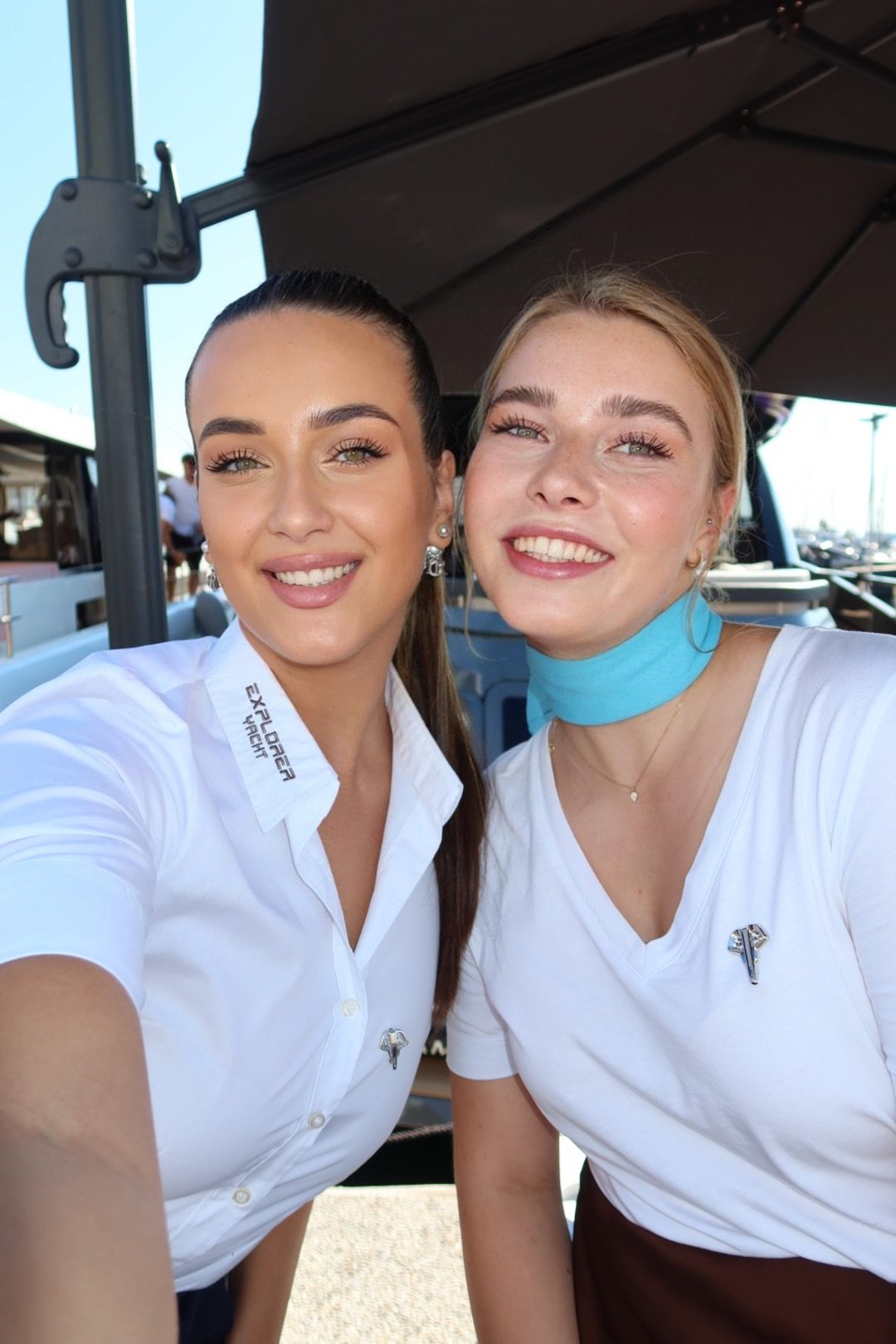 Two smiling women in professional yacht crew uniforms enjoying outdoor event